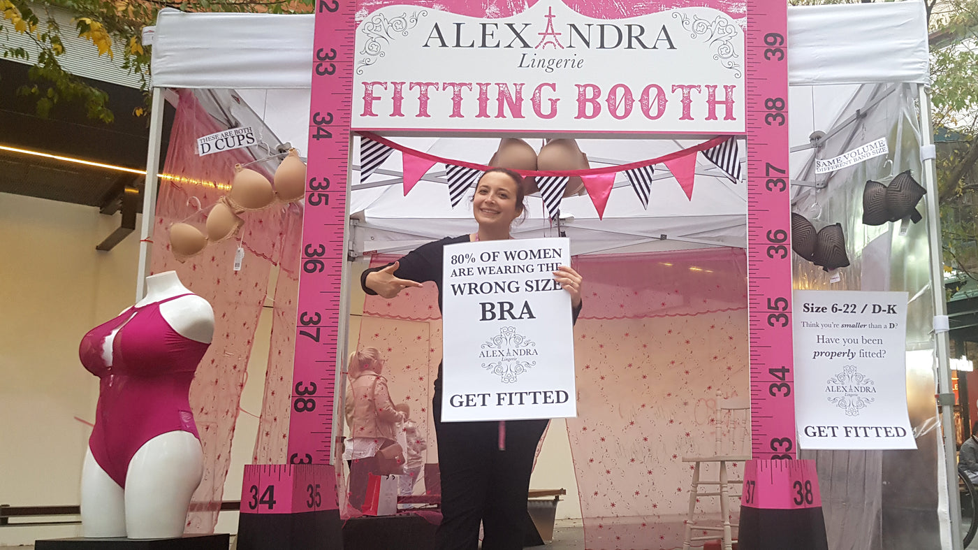 Alexandra, the store owner, showing off with a sign at the Alexandra Lingerie fitting booth. Hot pink tape measures and cute bunting decorate a marquee in Rundle Mall